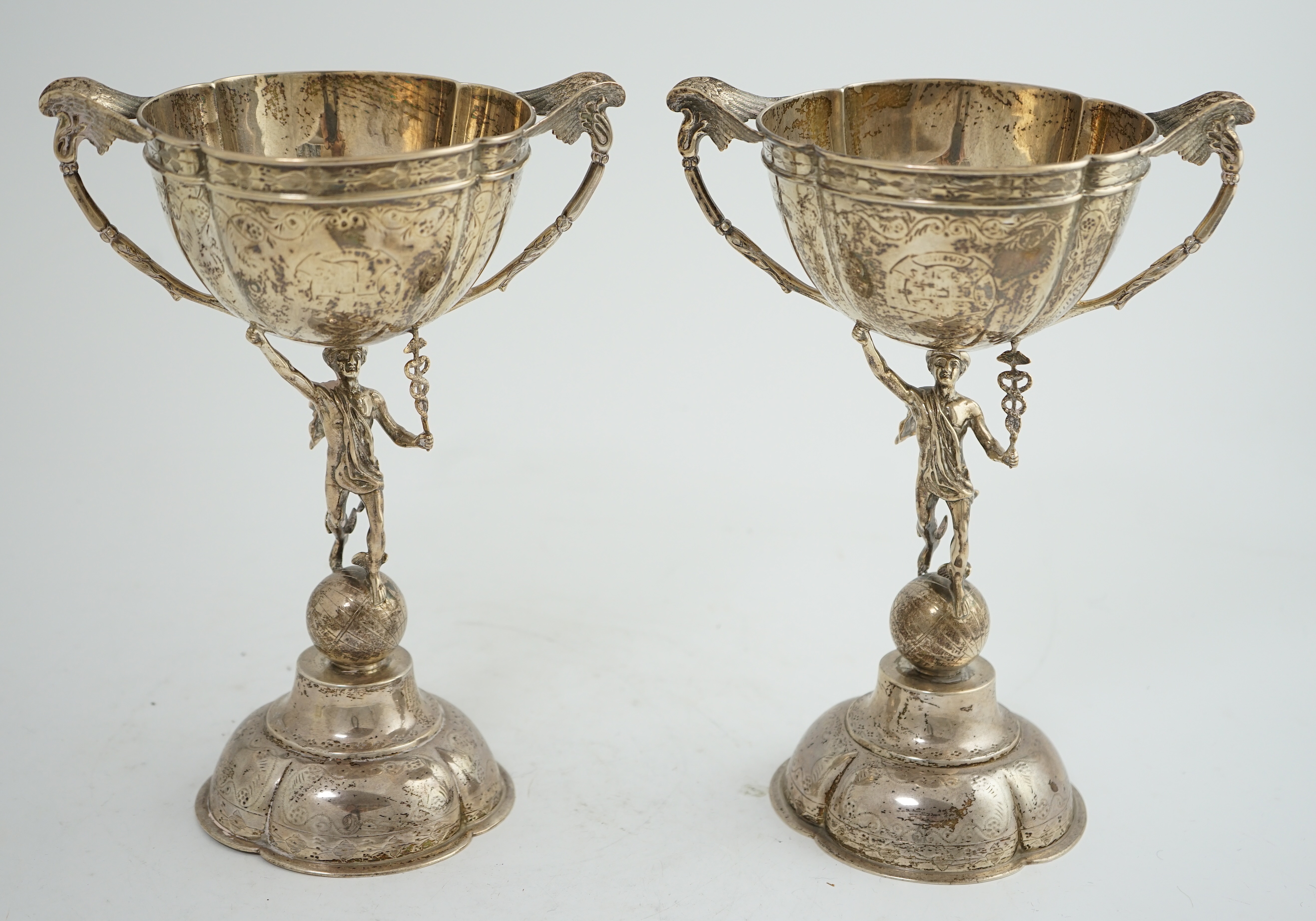 A pair of Victorian silver two handled pedestal cups, each figural stem modelled as Hermes upon a globe, by Edward Charles Brown